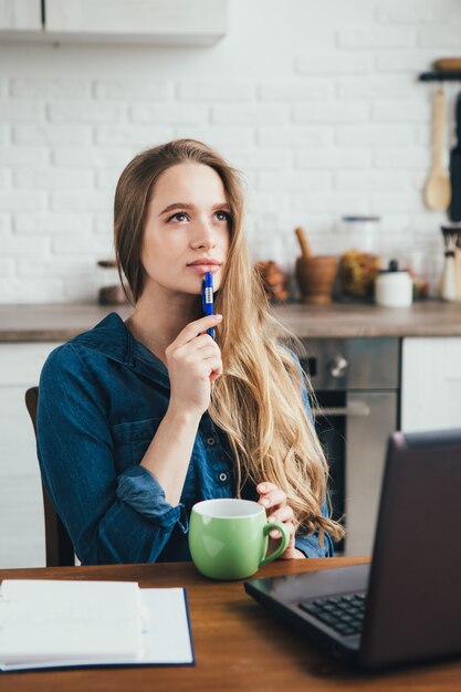 検疫で自己隔離のモードでキッチンで自宅で働くフリーランサーの若いかわいい妊娠中の女の子