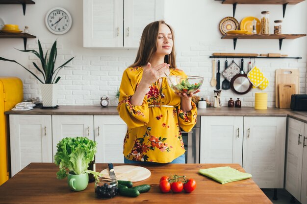 Молодая милая беременная девушка готовит овощной салат на кухне