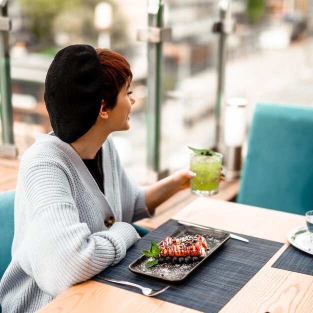 Young cute shorthaired girl drinking a basil smash cocktail or a lemonade at the summer terrace