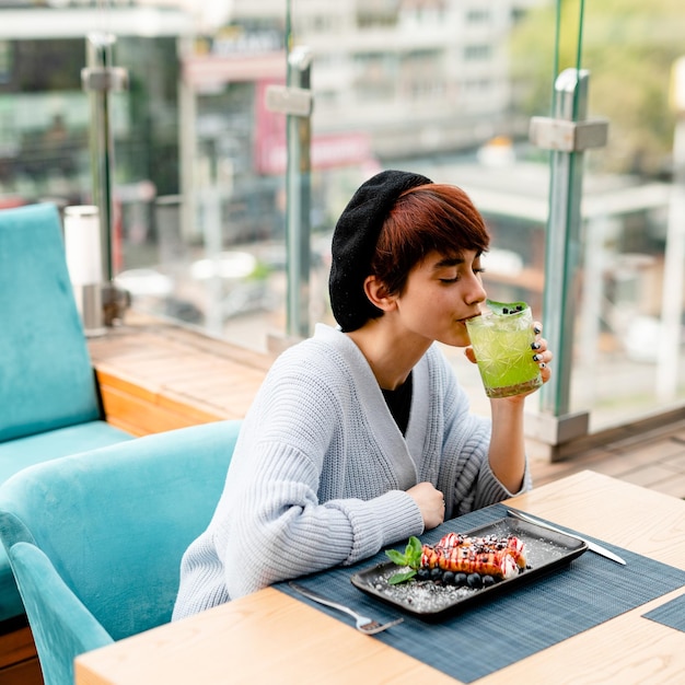 Young cute shorthaired girl drinking a basil smash cocktail or a lemonade at the summer terrace