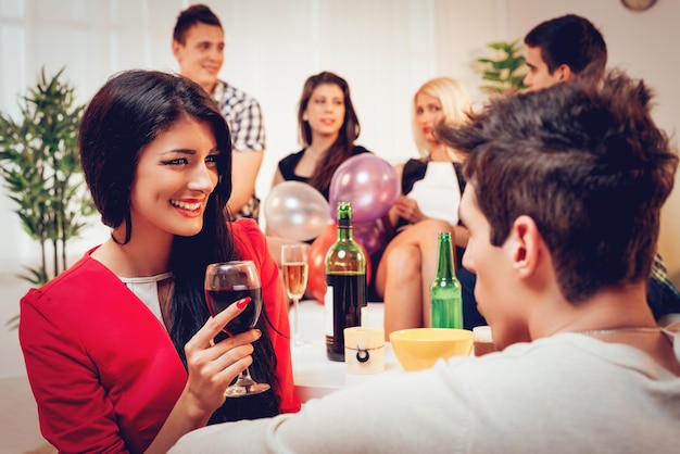 Young cute smiling girl holding a glass of wine on home party. She is looking at his boyfriend. Selective focus.