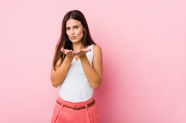 Young cute woman folding lips and holding palms to send air kiss.