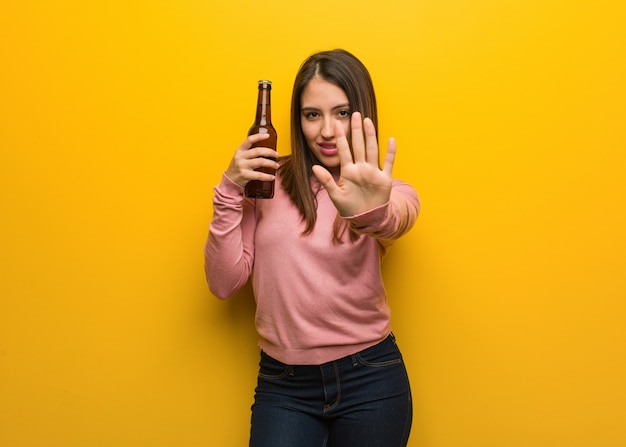 Young cute woman holding a beer putting hand in front