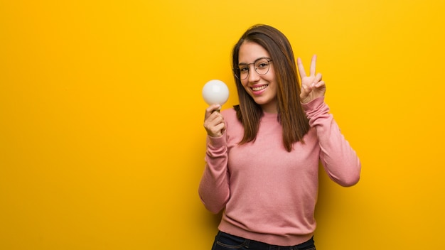 Young cute woman holding a light bulb fun and happy doing a gesture of victory