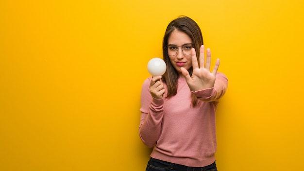 Giovane donna sveglia che tiene una lampadina che mette la mano nella parte anteriore