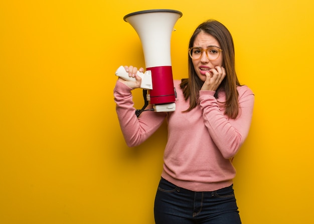 Young cute woman holding a megaphone biting nails, nervous and very anxious