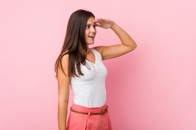 Young cute woman looking far away keeping hand on forehead.