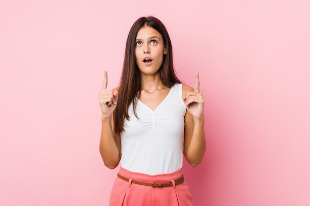 Young cute woman pointing upside with opened mouth.