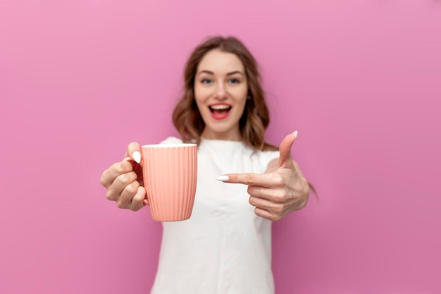 Photo young cute woman in white tshirt advertises cup with drink on pink background