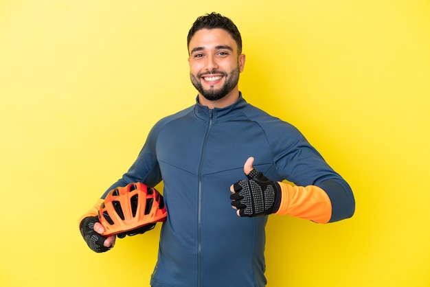 親指を立てるジェスチャーを与える黄色の背景に分離された若いサイクリストアラブ人