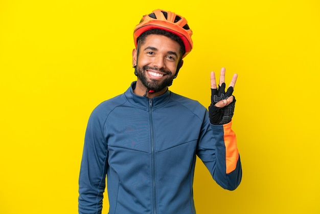 Giovane ciclista brasiliano uomo isolato su sfondo giallo felice e contando tre con le dita