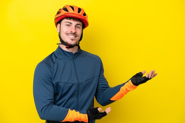 Young cyclist caucasian man isolated on yellow background extending hands to the side for inviting to come