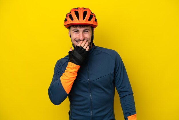 Young cyclist caucasian man isolated on yellow background happy and smiling covering mouth with hand