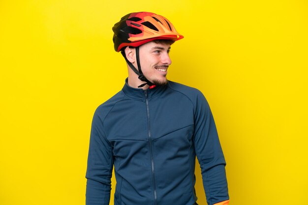 Young cyclist caucasian man isolated on yellow background looking to the side and smiling