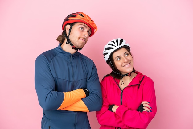 Young cyclist caucasian people isolated on pink background looking up while smiling