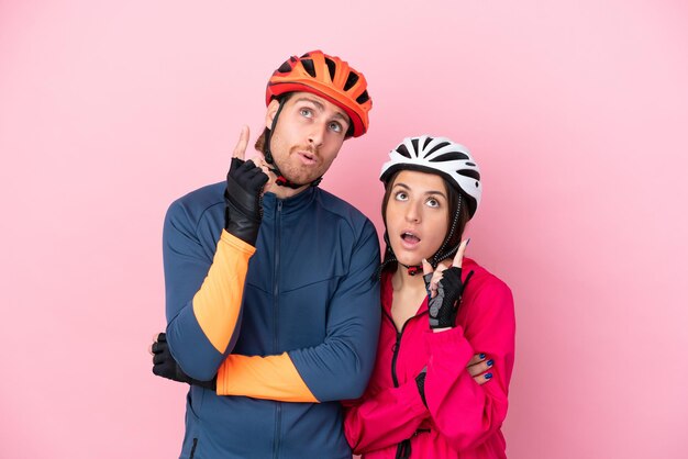 Young cyclist caucasian people isolated on pink background thinking an idea pointing the finger up