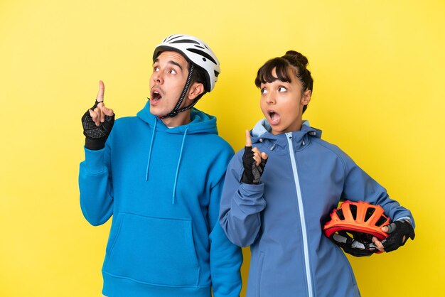 Young cyclist couple isolated on yellow background thinking an idea pointing the finger up