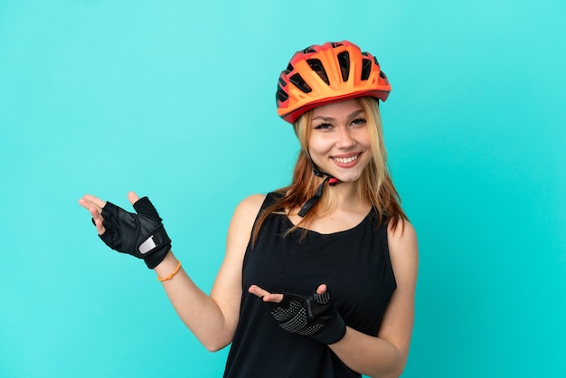 Ragazza giovane ciclista su sfondo blu isolato che estende le mani di lato per invitare a venire