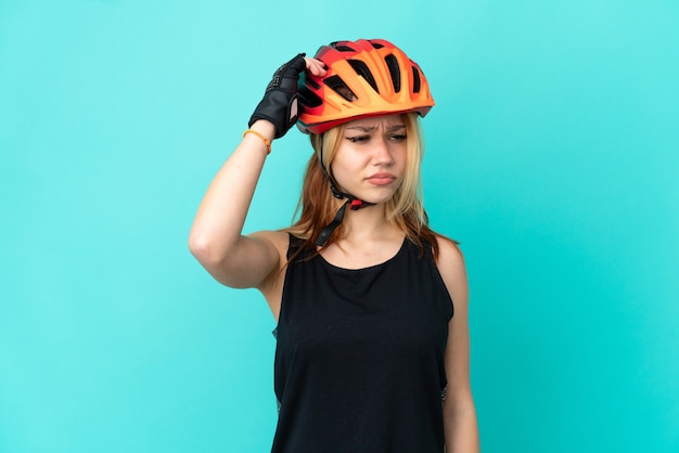 Young cyclist girl over isolated blue background having doubts while scratching head