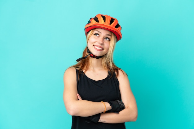 Young cyclist girl over isolated blue background looking up while smiling