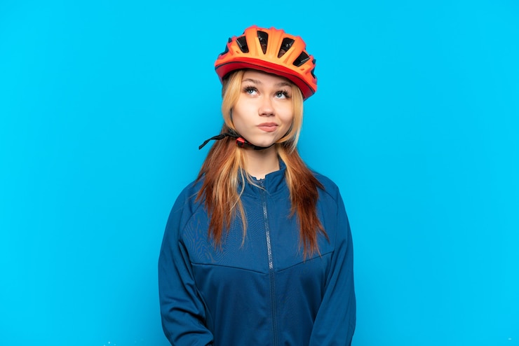 Photo young cyclist girl isolated on blue background and looking up