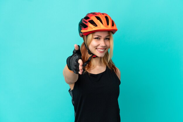 Young cyclist girl over isolated blue background shaking hands for closing a good deal