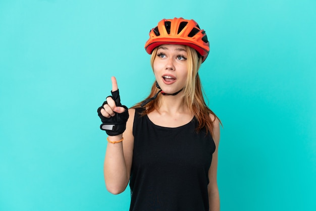 Young cyclist girl over isolated blue background thinking an idea pointing the finger up