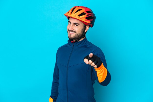 Young cyclist man isolated on blue background pointing front with happy expression