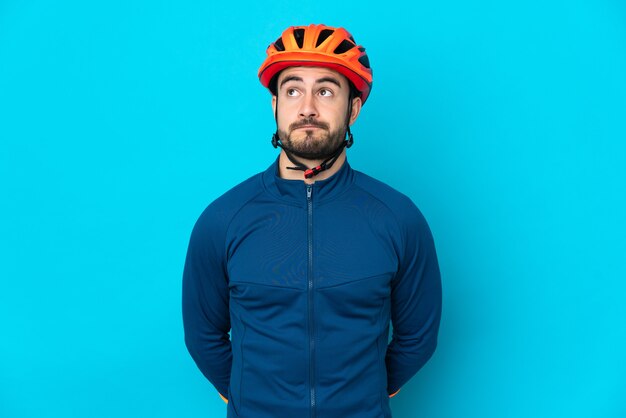 Young cyclist man isolated on blue wall and looking up