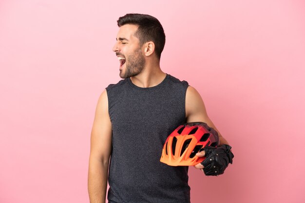 Young cyclist man isolated on pink background laughing in lateral position