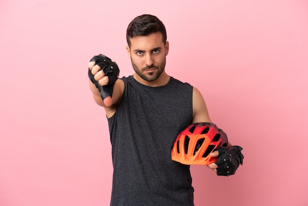 否定的な表現で親指を示すピンクの背景に分離された若いサイクリストの男