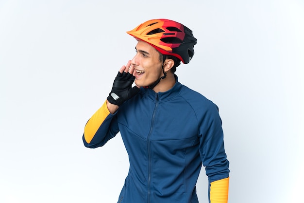 Young cyclist man isolated on wall shouting with mouth wide open to the side