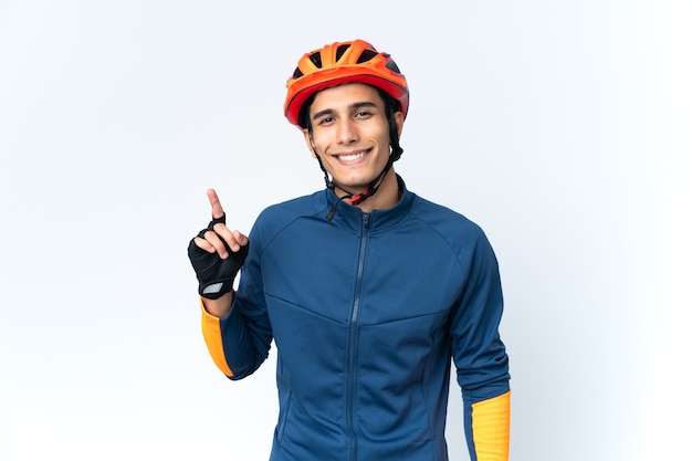 Young cyclist man isolated on wall showing and lifting a finger in sign of the best