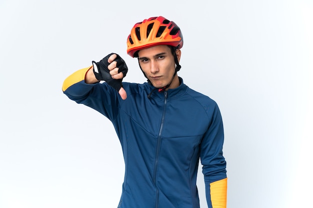 Молодой велосипедист мужчина изолирован на стене, показывая большой палец вниз с отрицательным выражением лица