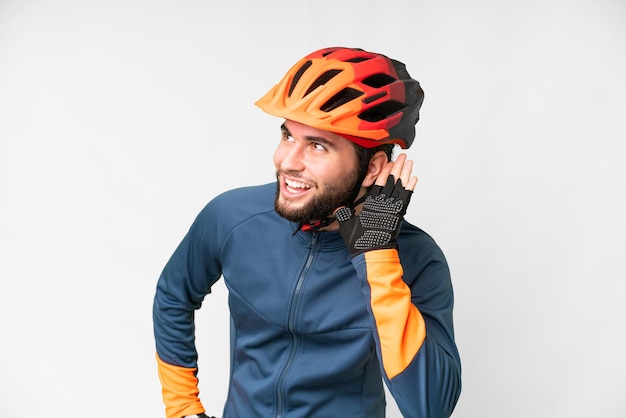 Foto giovane ciclista su sfondo bianco isolato ascoltando qualcosa mettendo la mano sull'orecchio