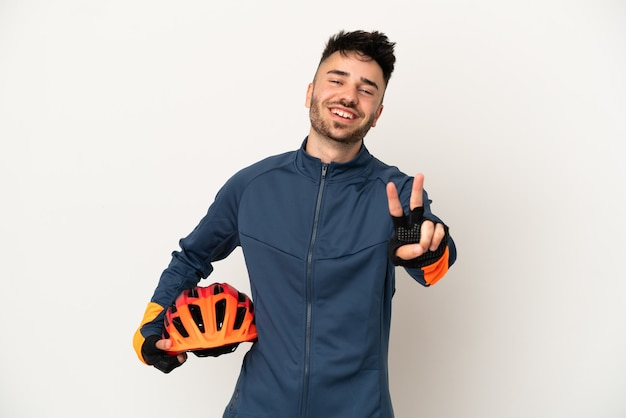 Young cyclist man isolated on white background smiling and showing victory sign