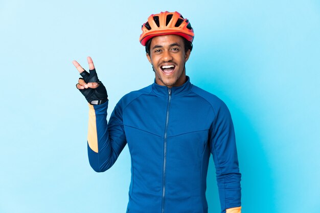 Young cyclist man with braids over isolated background smiling and showing victory sign