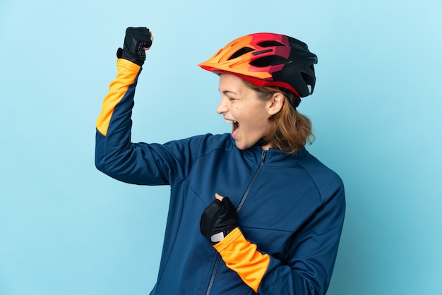 Donna giovane ciclista isolata su sfondo blu che celebra una vittoria