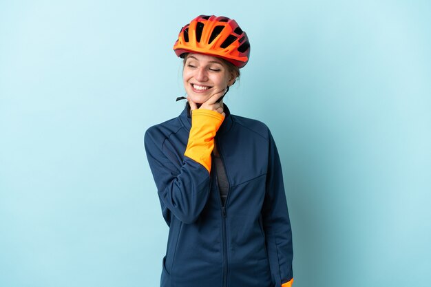 Young cyclist woman isolated on blue background looking to the side and smiling