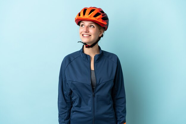 Young cyclist woman isolated on blue background thinking an idea while looking up