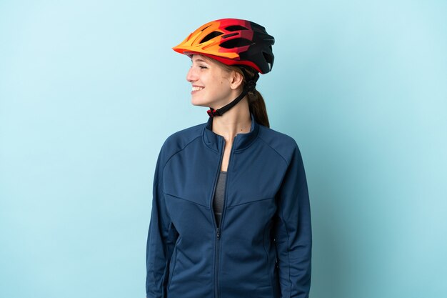 Young cyclist woman isolated on blue wall looking side