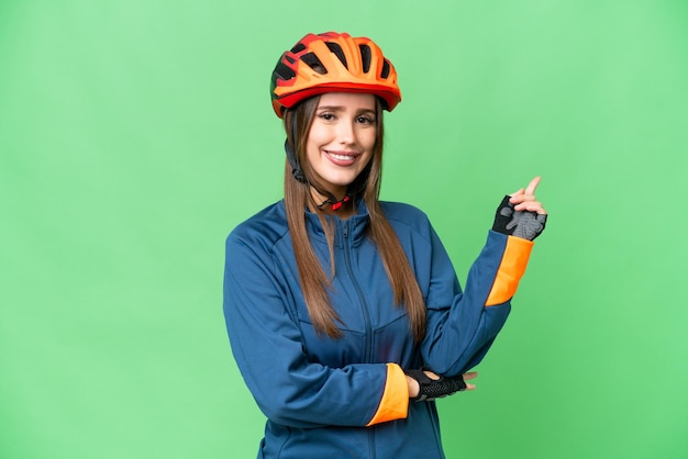 Young cyclist woman over isolated chroma key background pointing finger to the side