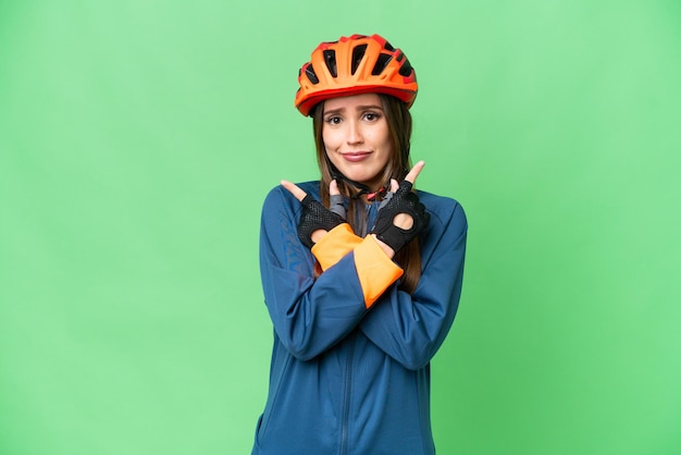 Young cyclist woman over isolated chroma key background pointing to the laterals having doubts