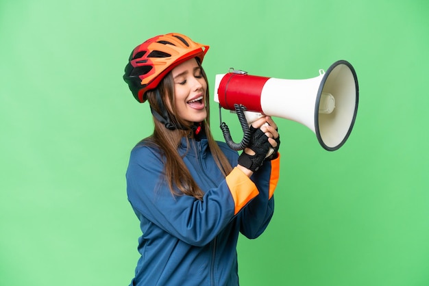 メガホンを通して叫んでいる孤立したクロマキーの背景の上の若いサイクリストの女性