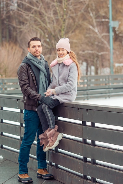 Young dad and adorable little girl have fun on skating rink outdoors