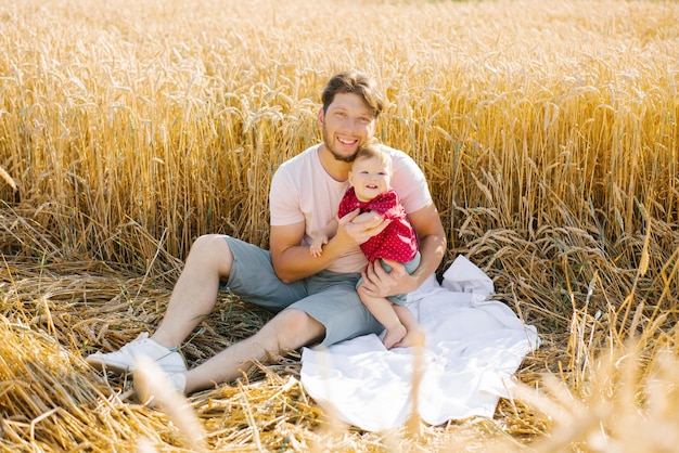 A young dad and his son are sitting in nature in the summer in the field