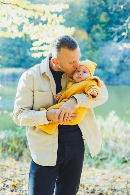 Foto il giovane padre e il figlio nel parco all'aperto il padre tiene e bacia suo figlio padre e figlio felici