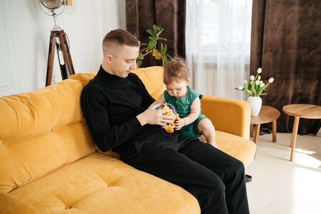 Foto un giovane padre gioca con il suo bambino su un divano giallo