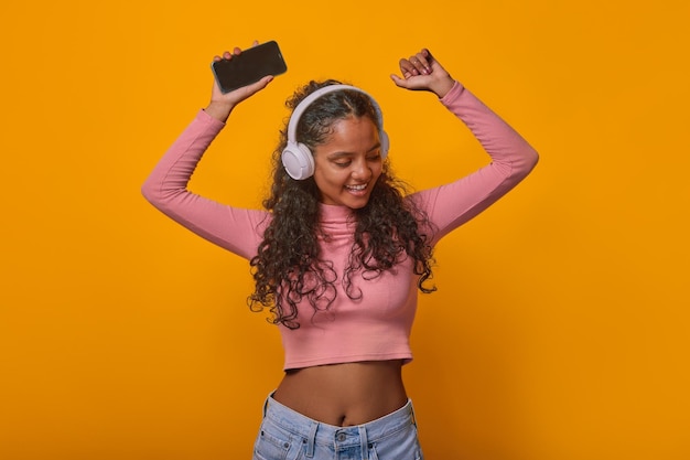 Giovane ragazza indiana che balla ascolta musica con le cuffie e tiene in mano il telefono