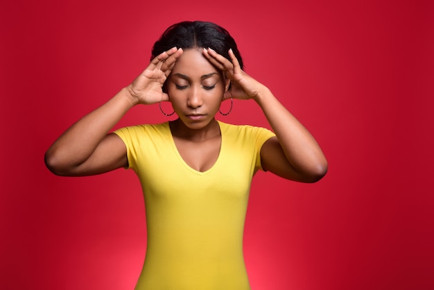 Young dark-skinned girl in a yellow T-shirt has a headache and holds her head in her hands.